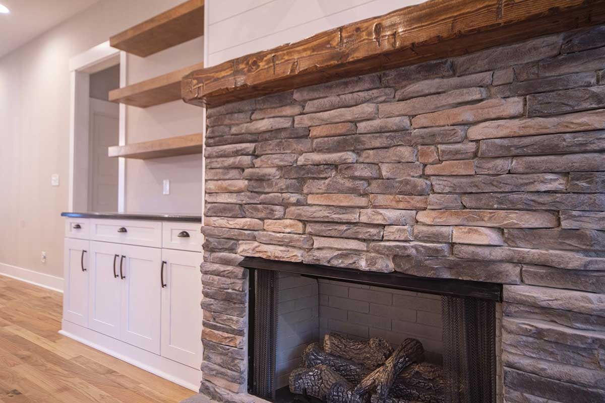 Stone fireplace with built-in white cabinets and wood mantel in a bright living room