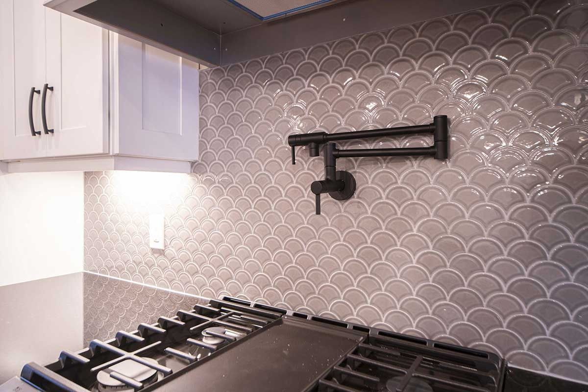 Modern kitchen corner with white cabinets, gas stove, and gray scalloped tile backsplash