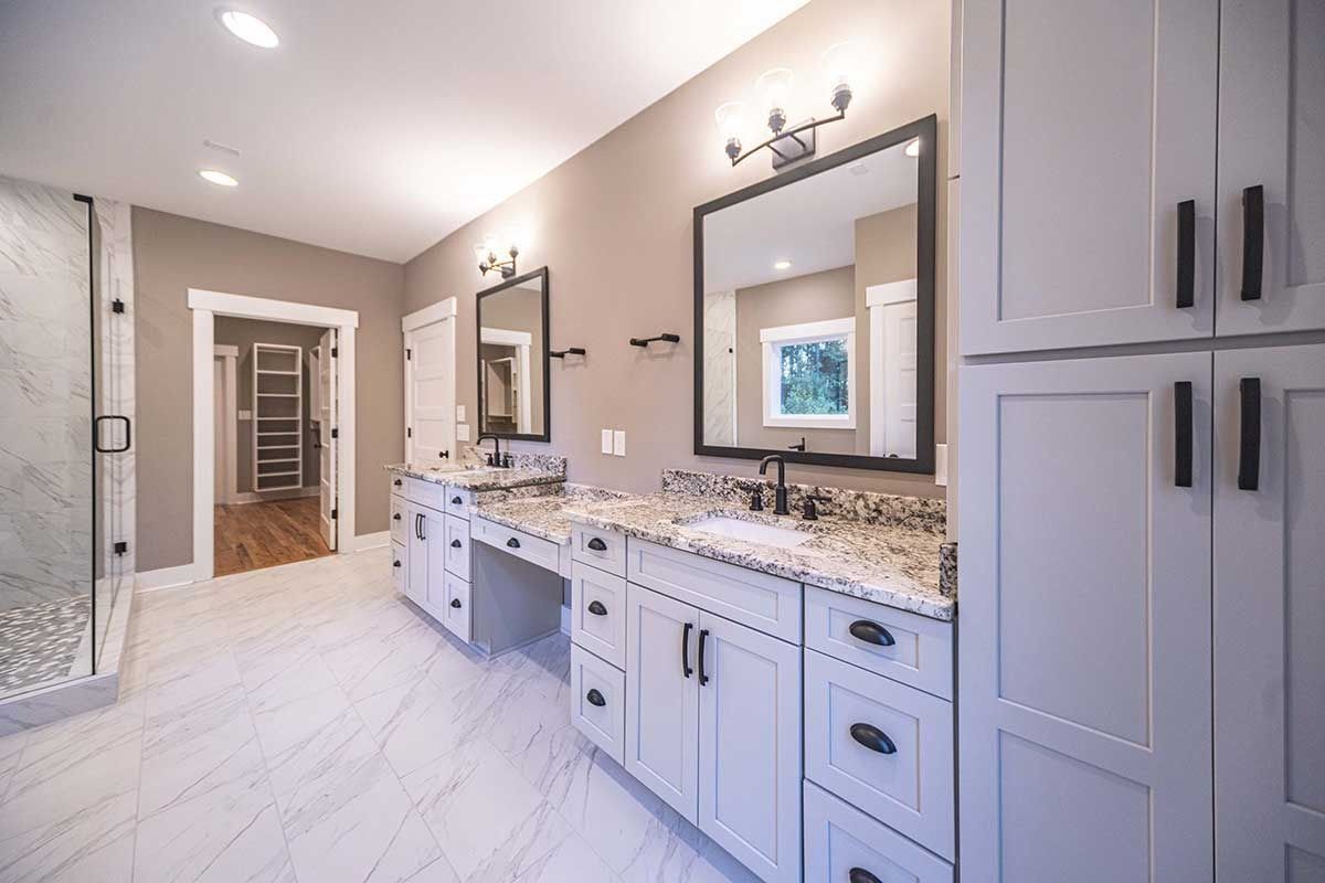Bright bathroom with double vanity, large mirrors, gray cabinets, and white tile flooring.