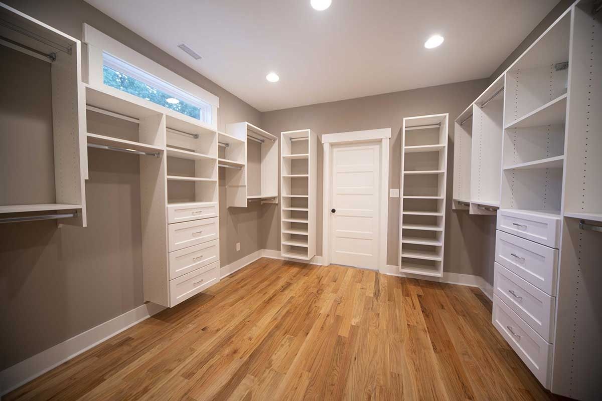 Bright empty walk-in closet with white shelving, drawers, and wood flooring