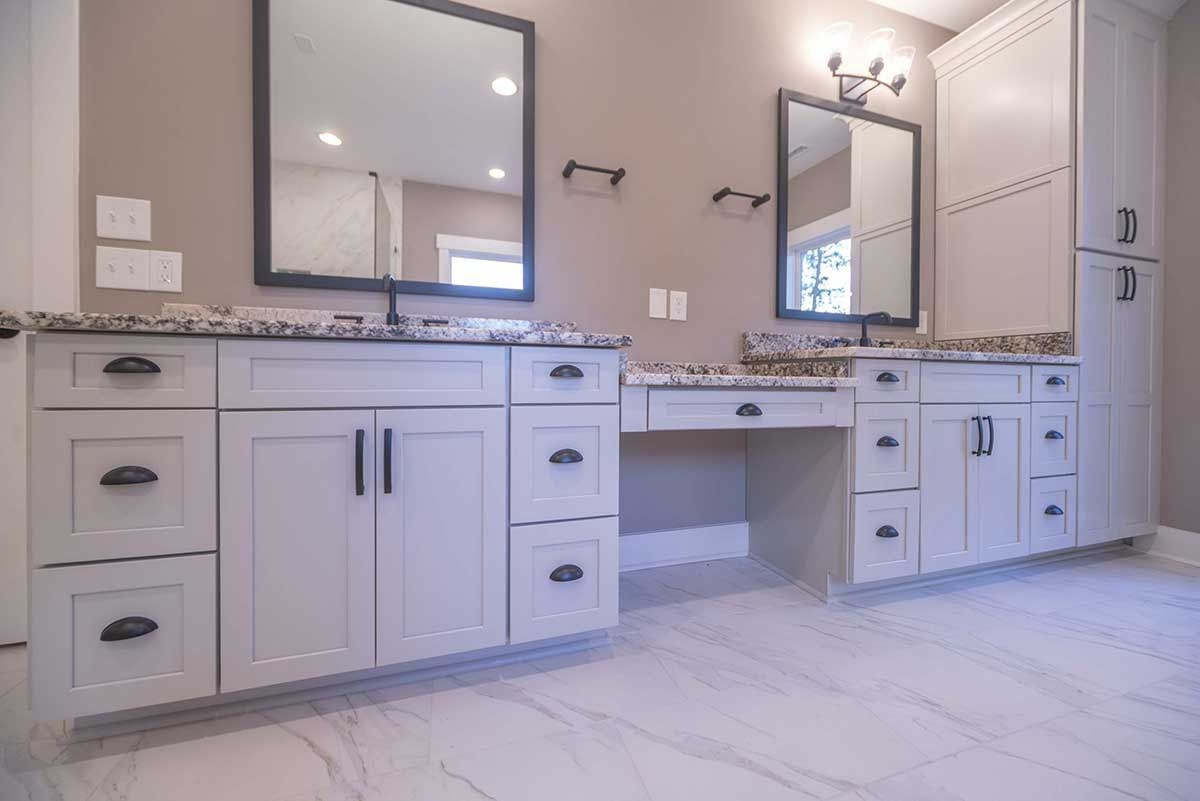 Modern double vanity bathroom with white cabinets, marble counters, mirrors, and wall sconces