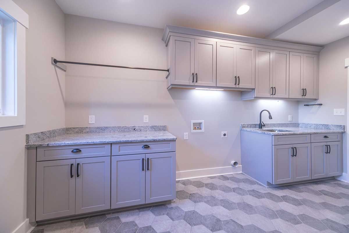 Empty modern kitchen with gray cabinets, granite counters, white walls, and patterned tile floor.