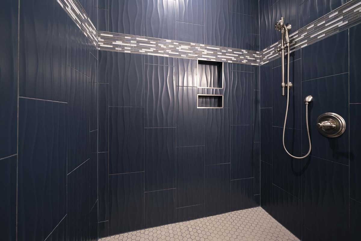 Dark blue tiled shower with a rainfall showerhead, handheld sprayer, and bench seat