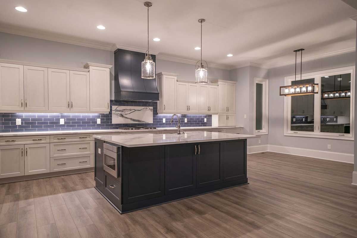 Spacious modern kitchen with white cabinets, dark island, pendant lights, and wood-look tile floor