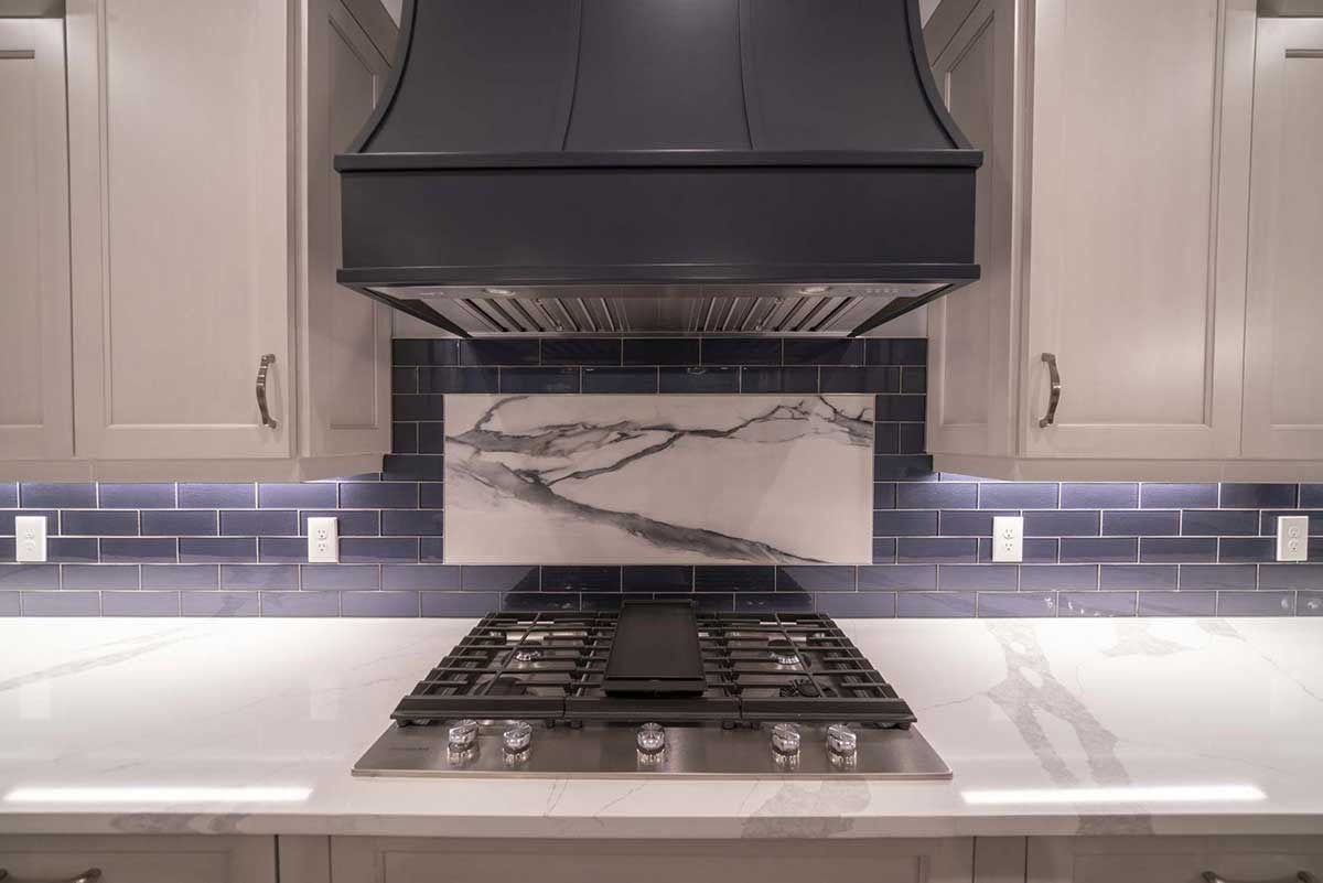 Modern kitchen with gas cooktop, black range hood, and white cabinets with marble backsplash