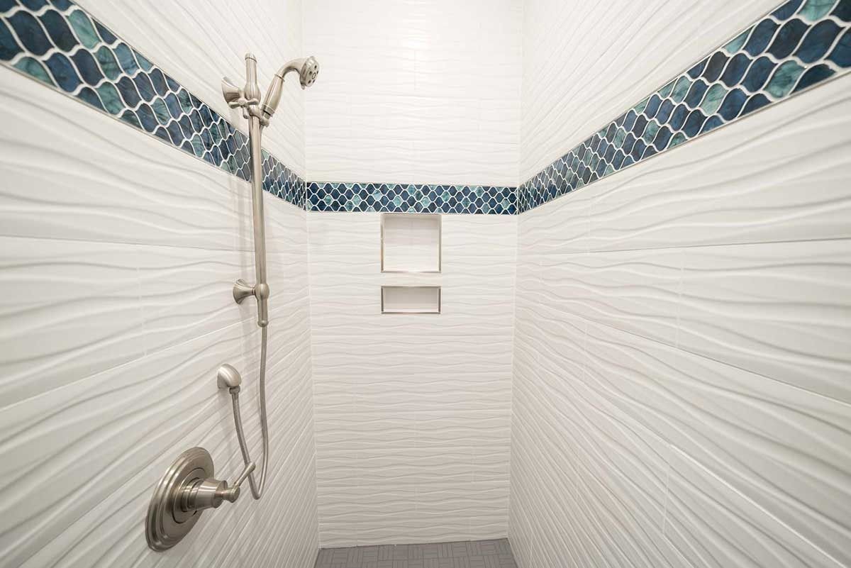 Walk-in shower with white textured walls, blue tile border, and chrome shower fixtures