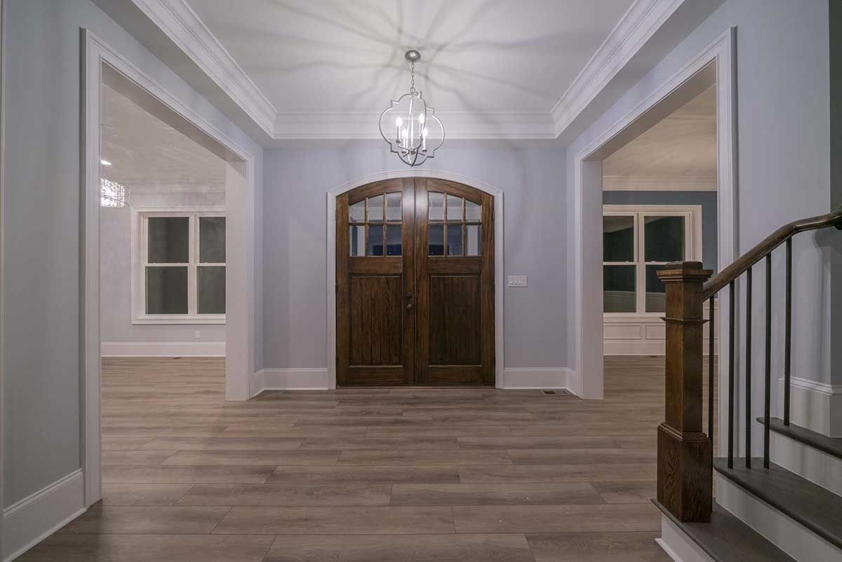 Bright entry hallway with wood floors, double front doors, windows, and a staircase railing on the right