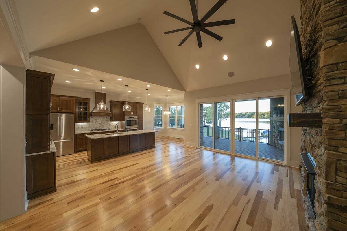 Open-concept kitchen and living room with hardwood floors, stone fireplace, and sliding doors to a patio.