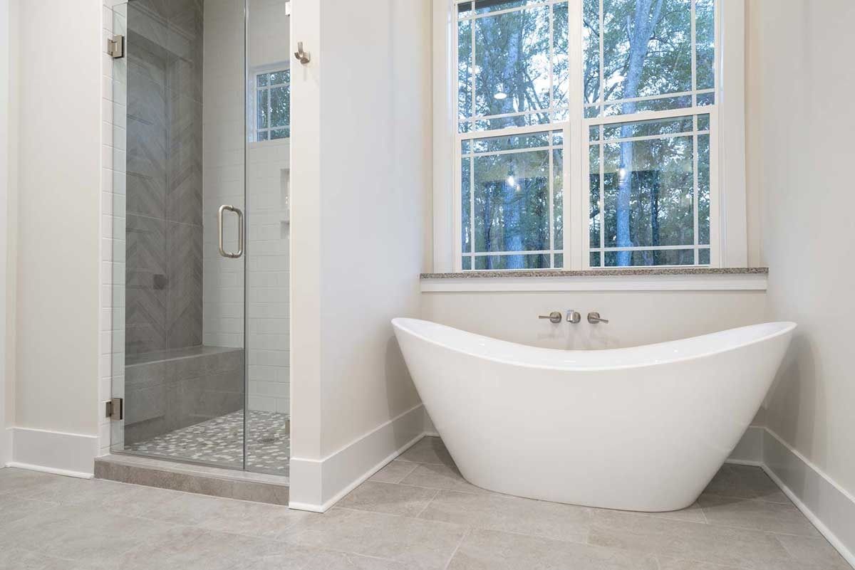 Modern bathroom with freestanding white tub, glass shower, and large window