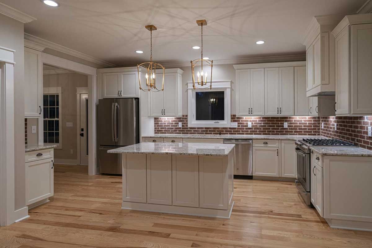Spacious modern kitchen with white cabinets, marble island, stainless fridge, and wood floors