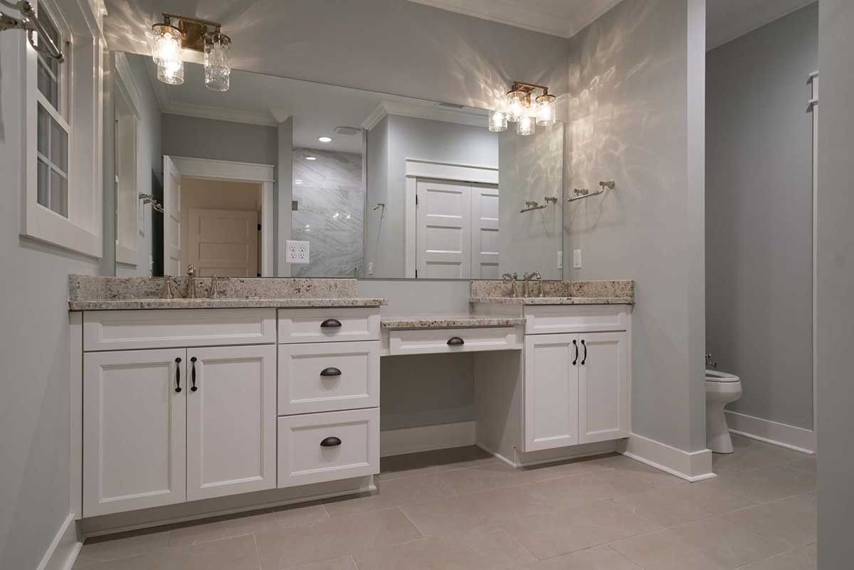 Bright bathroom vanity with double sinks, large mirror, and white cabinets in a gray room