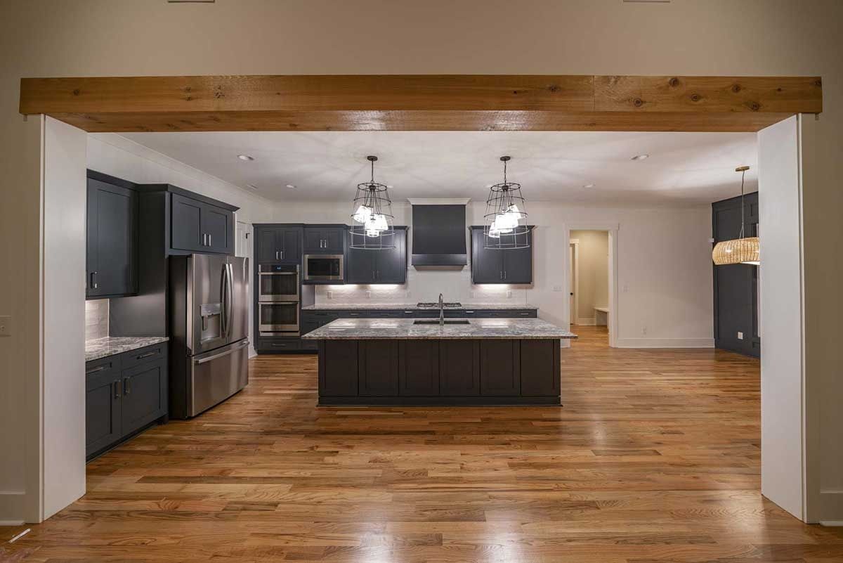 Modern kitchen with dark cabinets, stainless appliances, wood floors, and an island under exposed beams