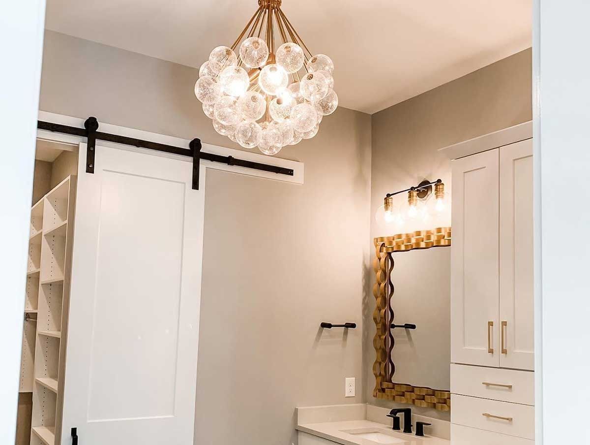 Modern bathroom with white sliding barn door, ornate mirror, and crystal chandelier