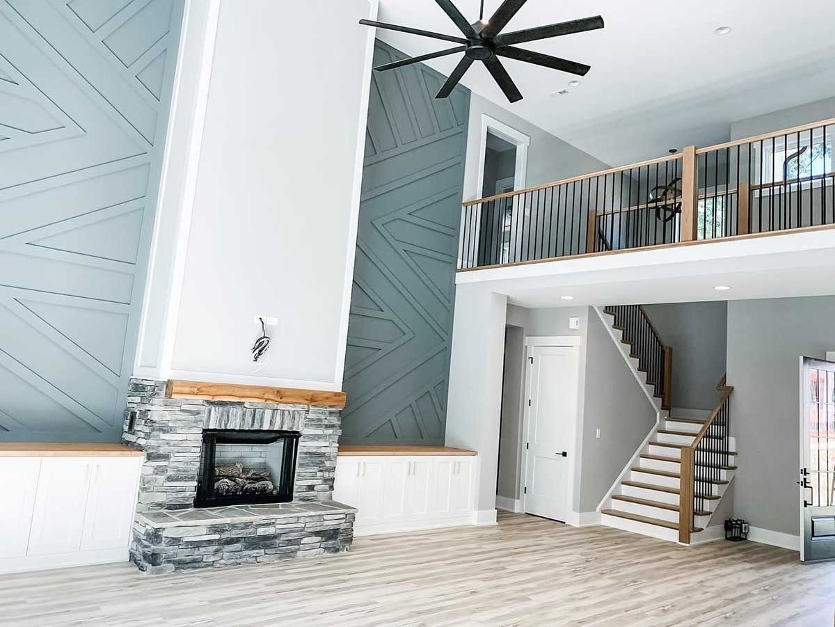 Bright modern living room with a stone fireplace, vaulted ceiling fan, loft balcony, and staircase