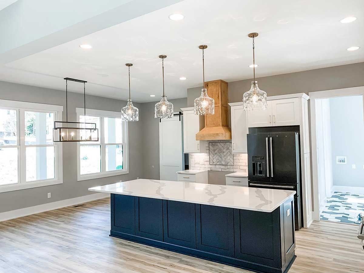 Bright modern kitchen with navy island, white cabinets, pendant lights, and stainless steel fridge