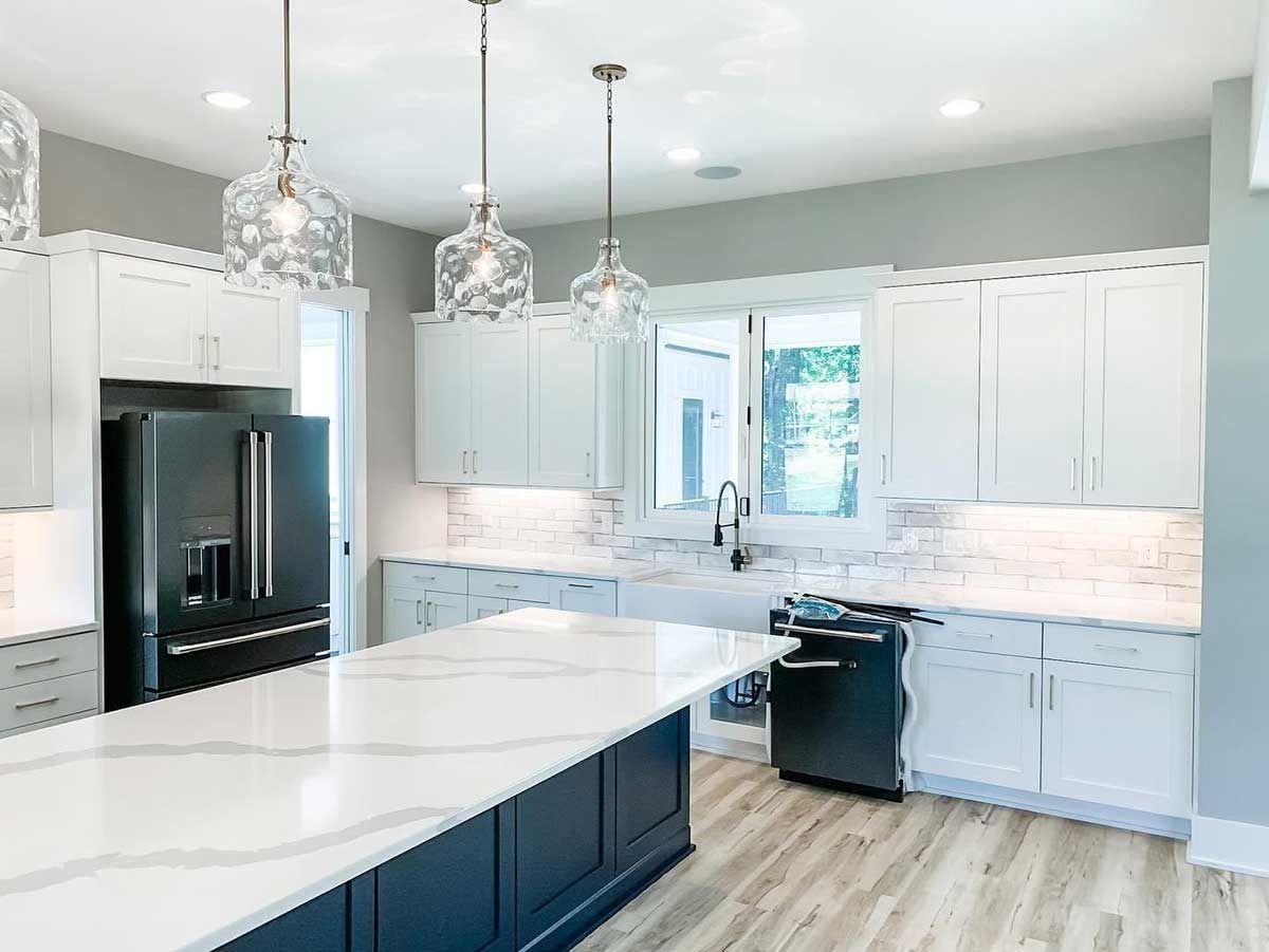Bright modern kitchen with white cabinets, marble island, black refrigerator, and pendant lights