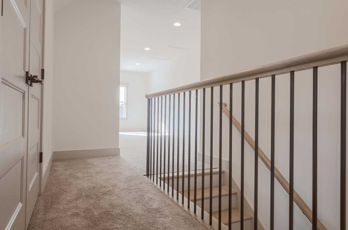 Carpeted upstairs hallway with white walls and a black metal stair railing