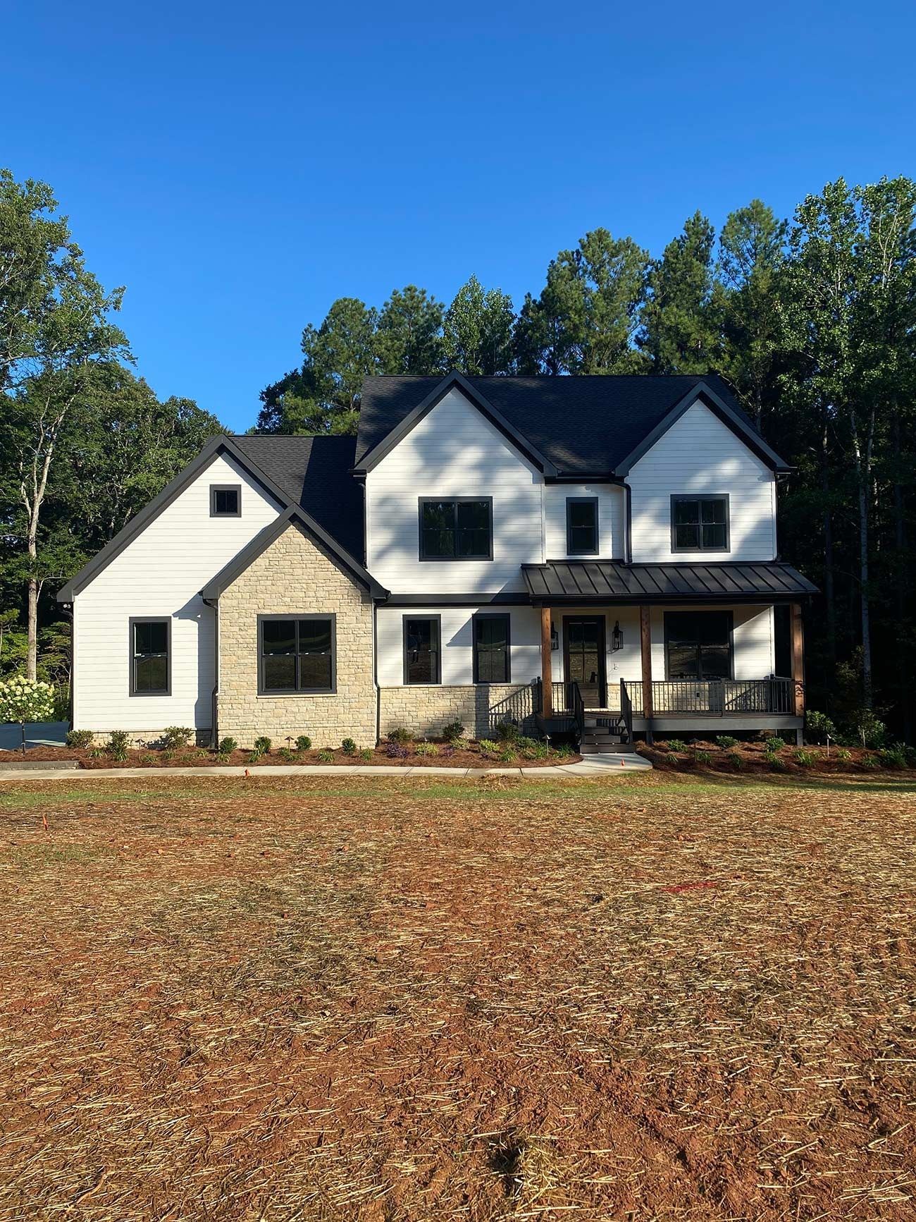 Two-story white house with dark roof and front porch, viewed from a leaf-covered yard under a blue sky
