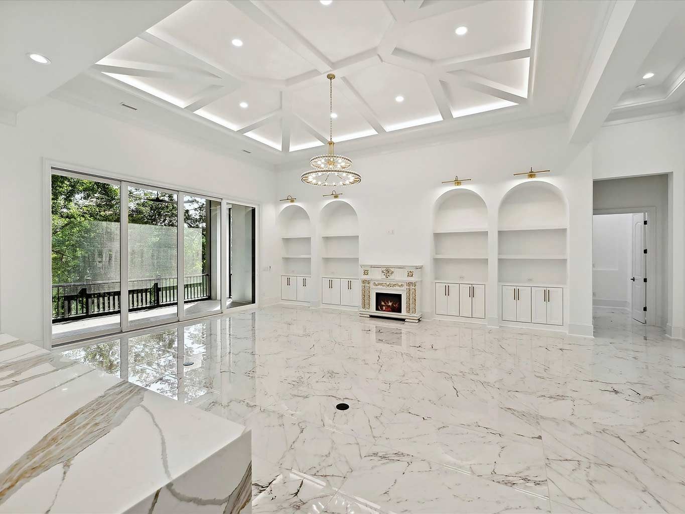 Bright white luxury living room with marble floors, built-in shelves, fireplace, and large sliding glass doors