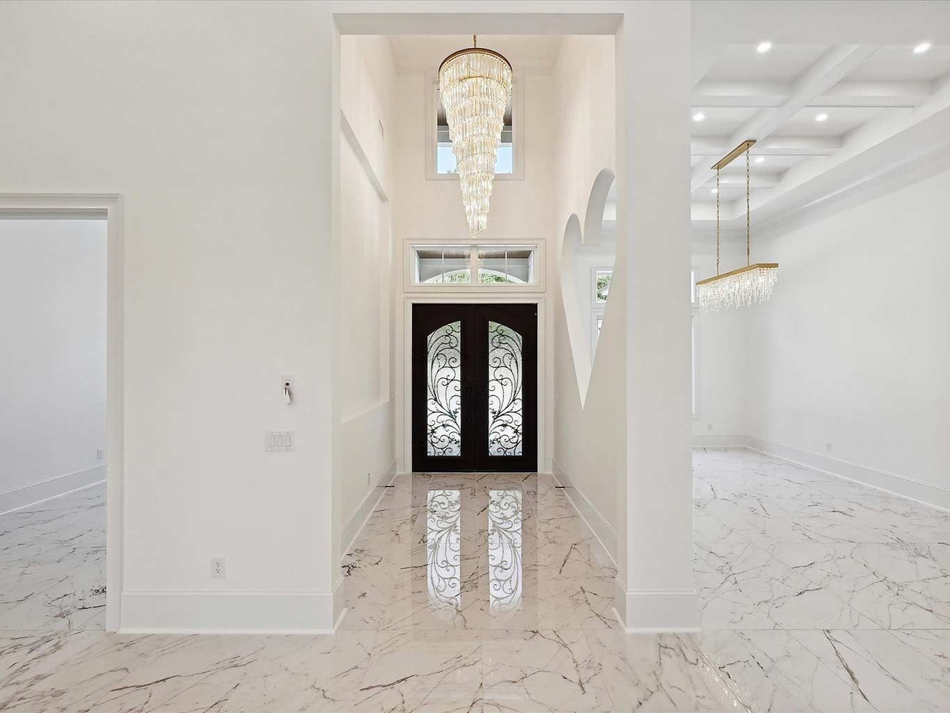 Bright white marble foyer with double black front doors and a crystal chandelier