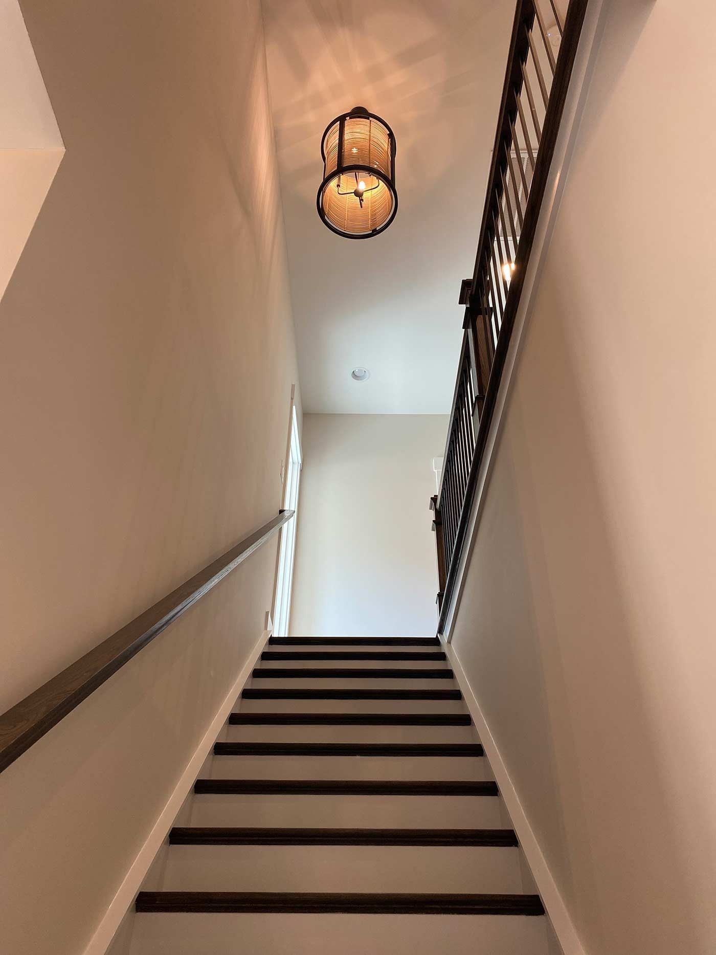 Narrow staircase with white walls, dark steps, and a hanging lantern light above.