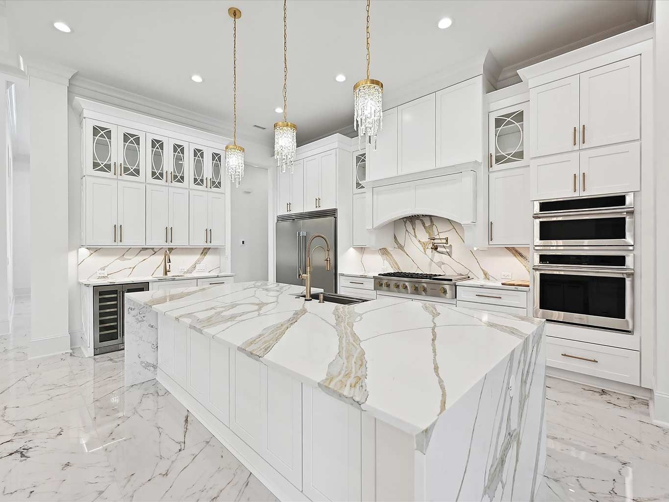 Bright white luxury kitchen with marble island, gold pendant lights, and built-in stainless steel appliances