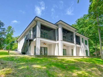 Modern two-story white house with dark trim, balconies, and a grassy yard surrounded by trees