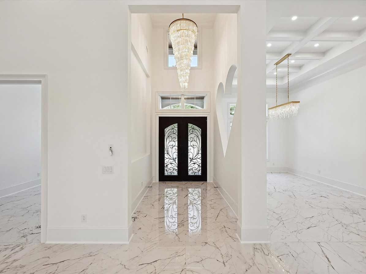 Bright foyer with chandelier, black double front doors, and polished marble floors leading into a white interior.