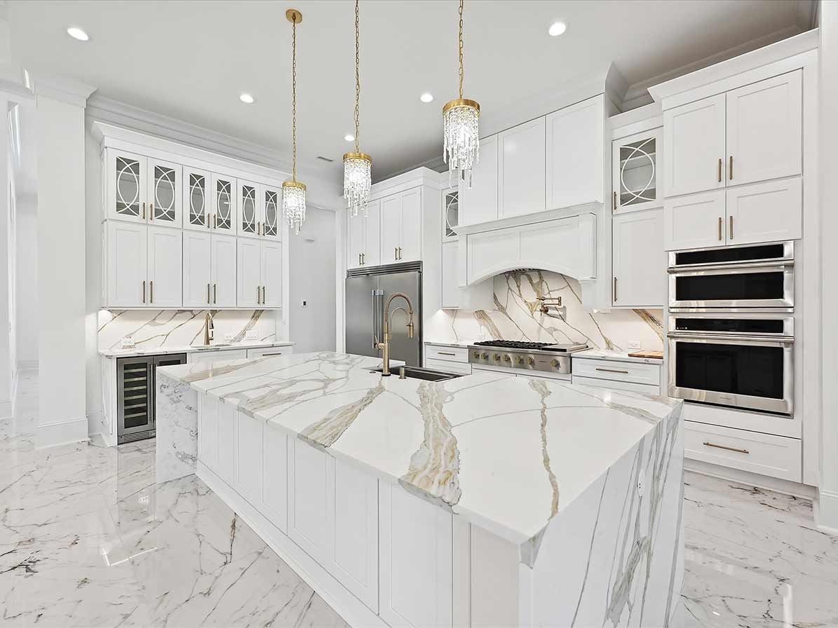 Bright white luxury kitchen with marble island, gold pendant lights, and built-in ovens