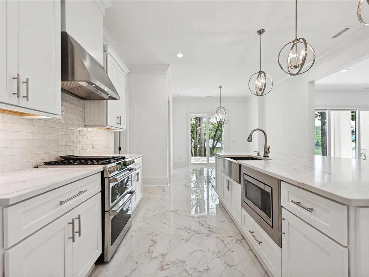 Bright white modern kitchen with marble floors, stainless steel appliances, and pendant lights.