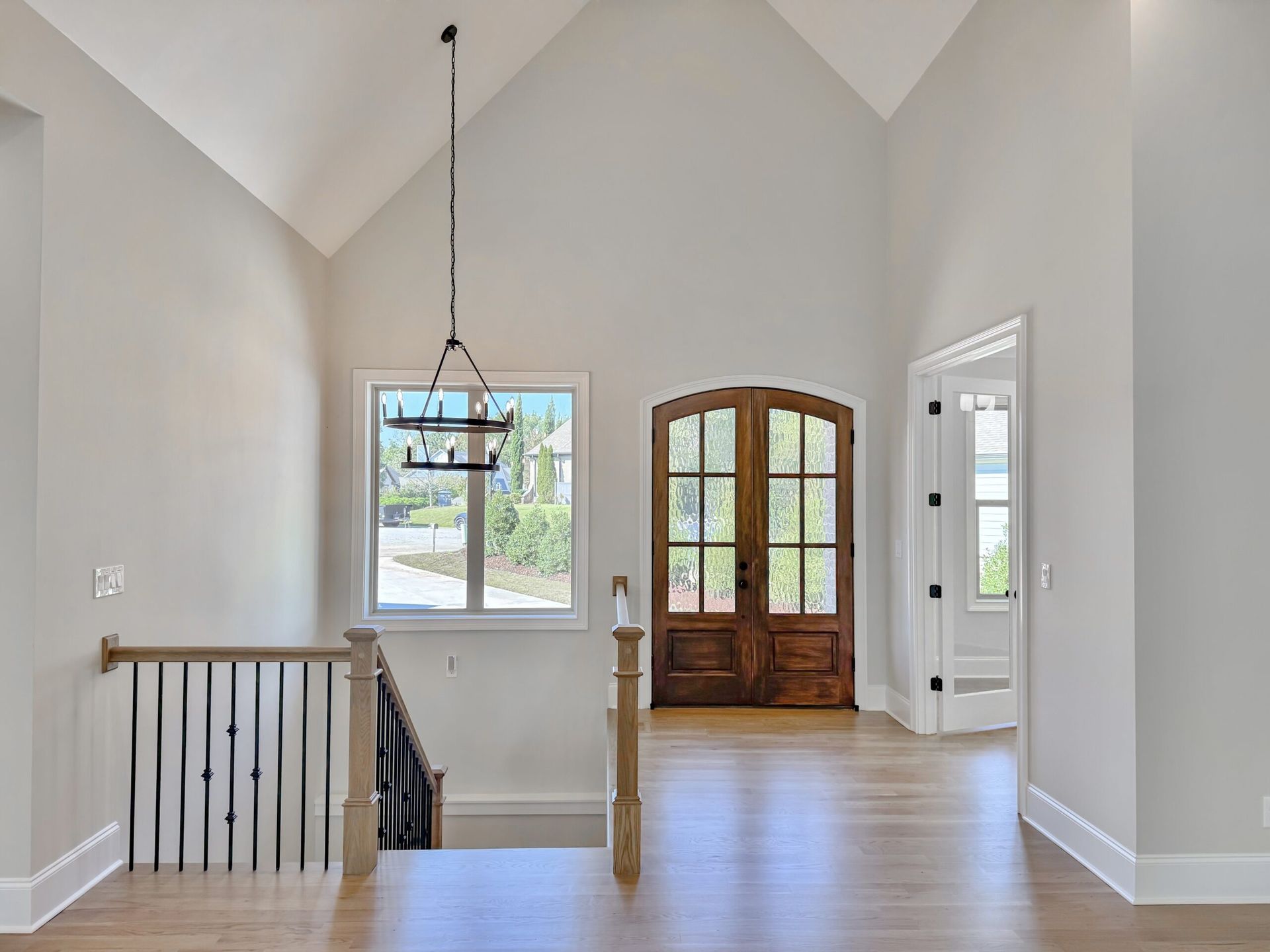 Bright entryway with vaulted ceiling, wood front door, window, and staircase railing