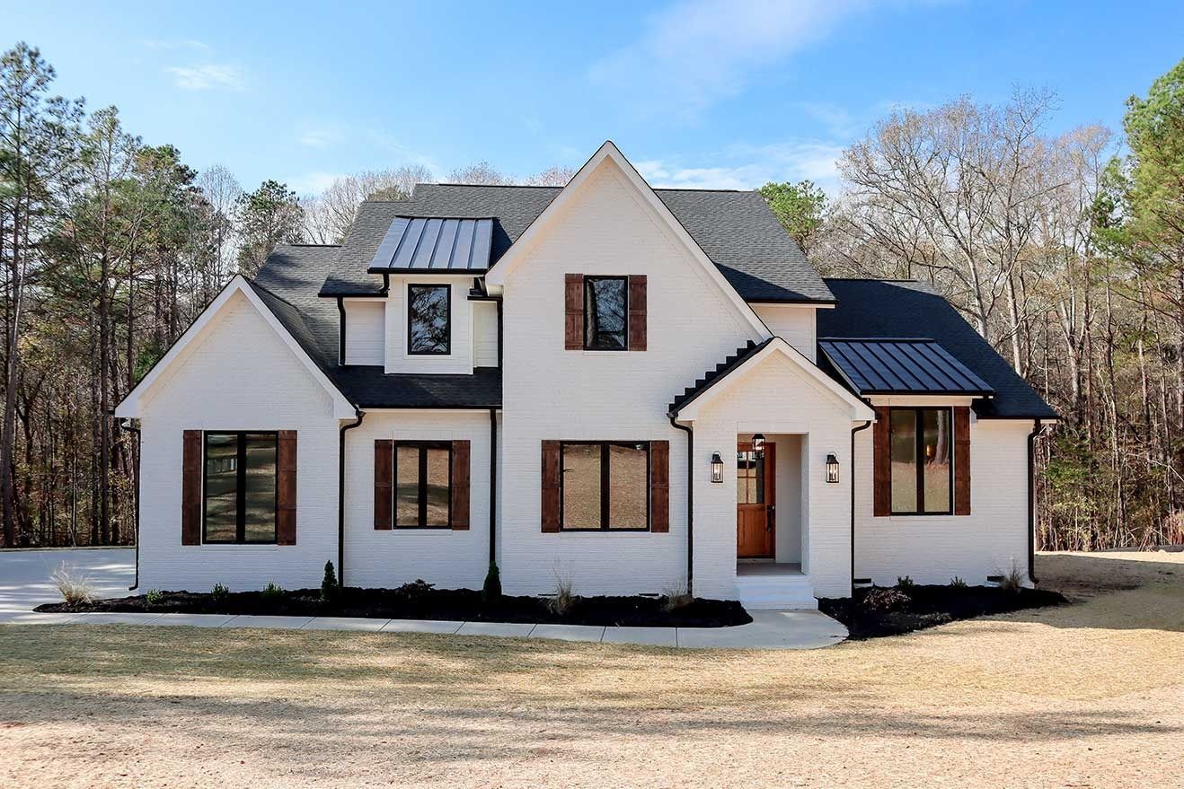 White stucco house with dark roof and brown trim, surrounded by trees under a blue sky