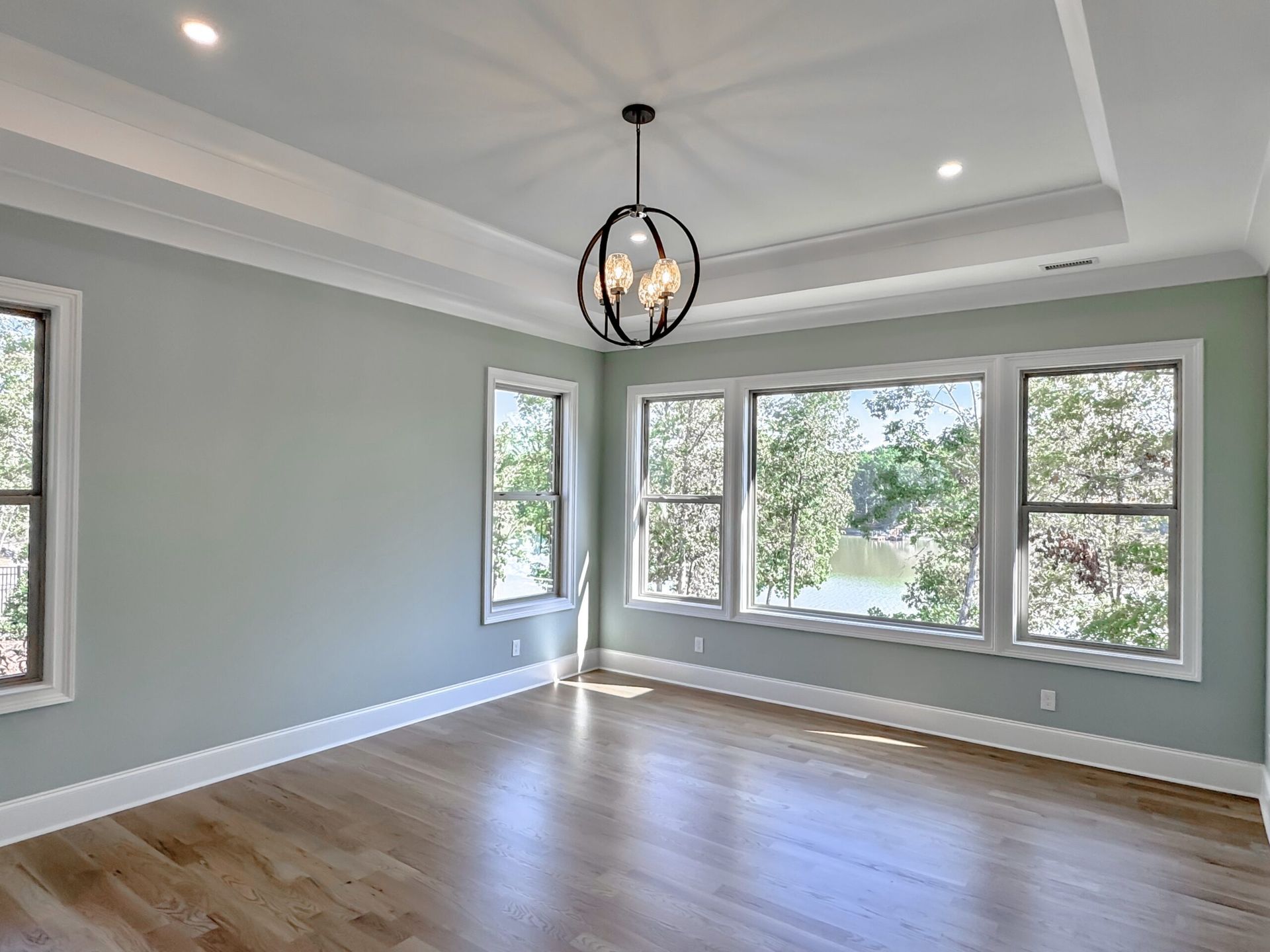 Bright empty living room with hardwood floor, gray walls, and large windows under a black pendant light