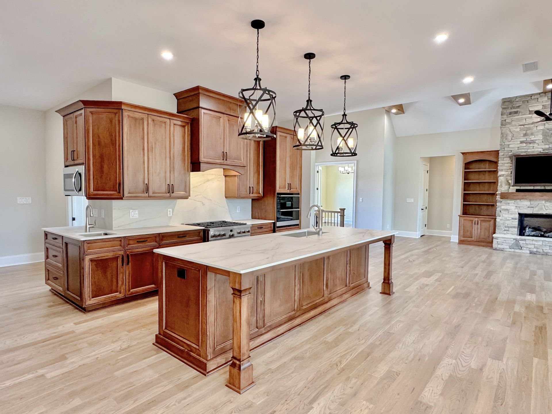 Spacious modern kitchen with wood cabinets, granite island, pendant lights, and open living area