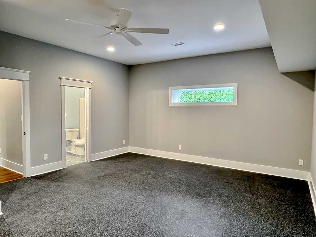 Empty gray bedroom with carpet, ceiling fan, two doorways, and a small window high on the wall