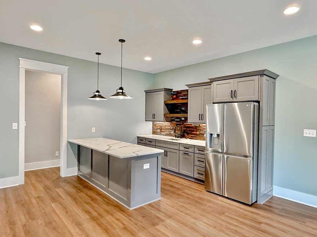 Modern kitchen with stainless steel appliances, gray cabinets, and a marble island under pendant lights