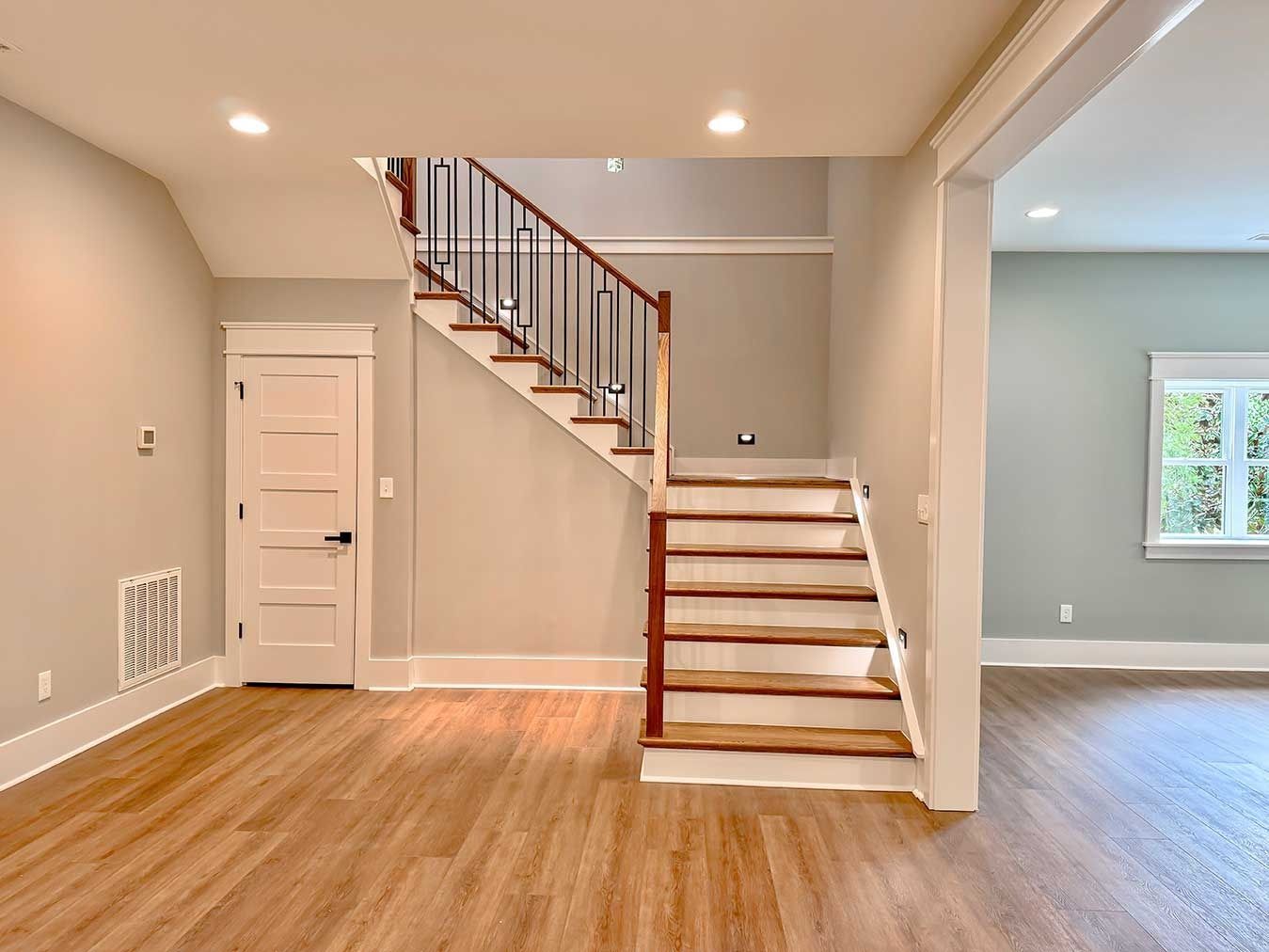 Empty living room with light wood floors, beige walls, and a staircase with white railings and wood steps
