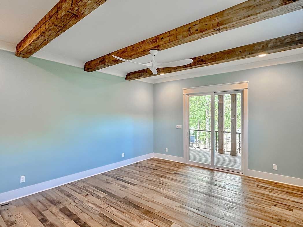 Empty room with wood beams, light blue walls, hardwood floors, and sliding glass doors to a balcony