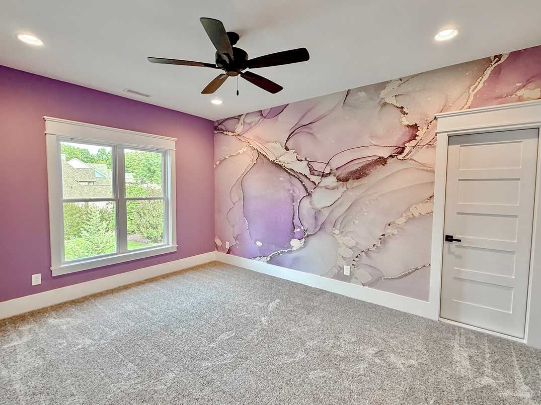 Empty bedroom with lavender walls, floral accent mural, gray carpet, and a white door and window.