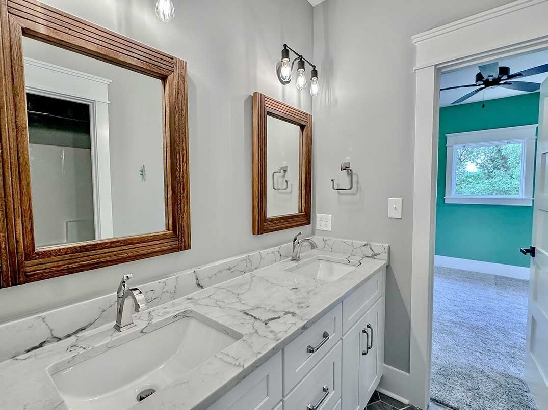 Bathroom vanity with two sinks, marble countertop, and mirrors; doorway opens to a teal bedroom.