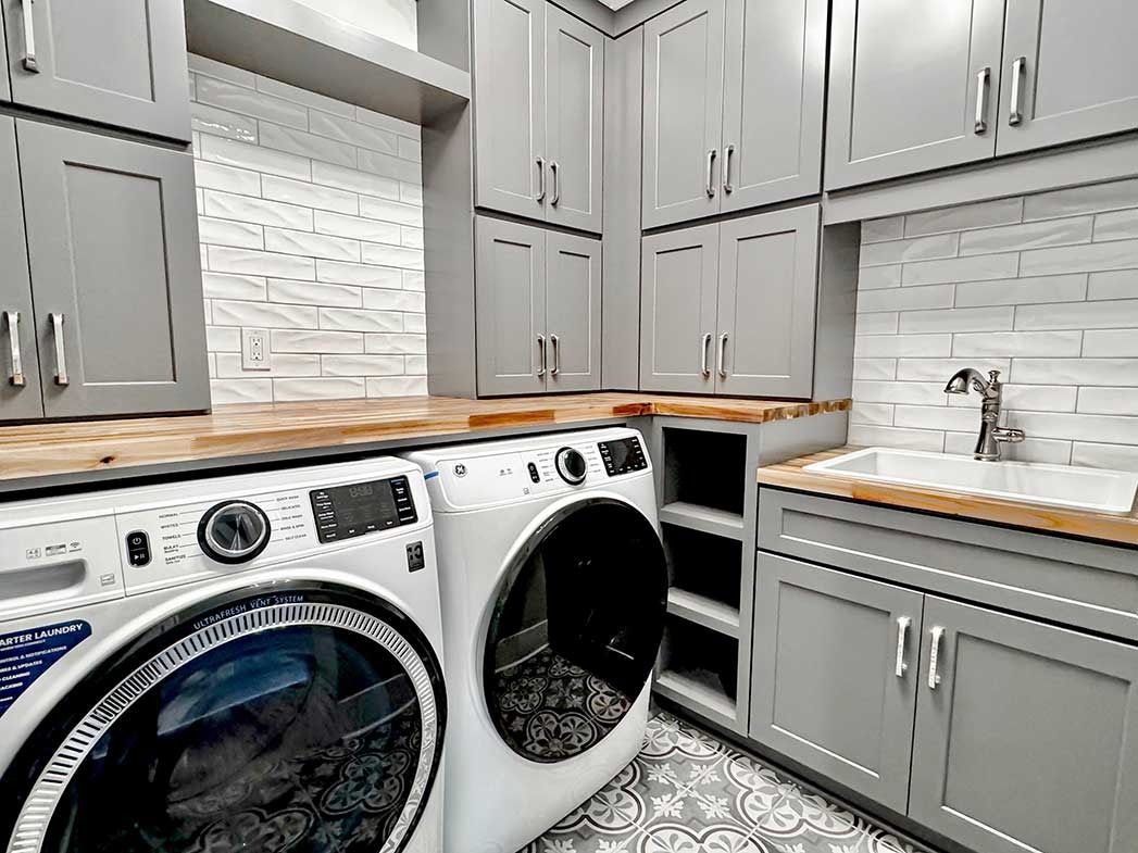 Laundry room with gray cabinets, white washer and dryer, wood countertop, and sink