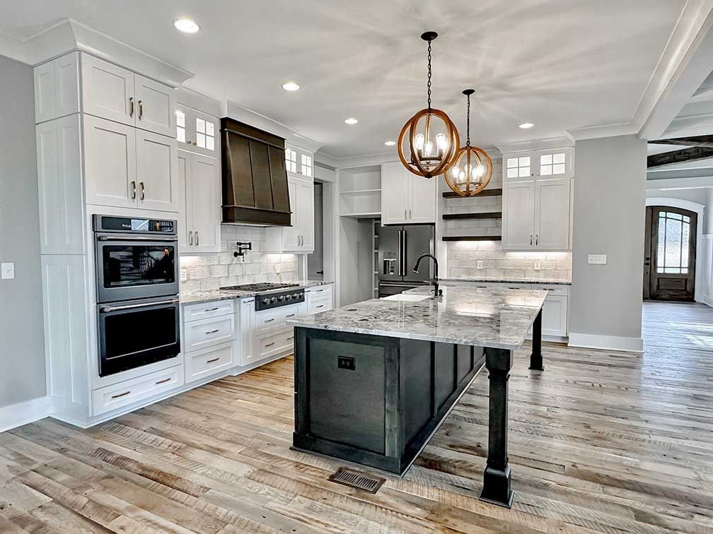 Bright modern white kitchen with island, wood floors, stainless appliances, and pendant lights.
