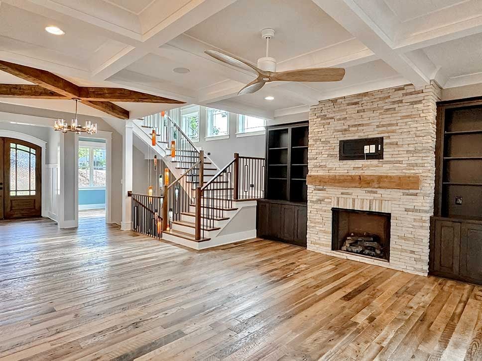 Bright living room with hardwood floors, vaulted ceiling, staircase, and stone fireplace