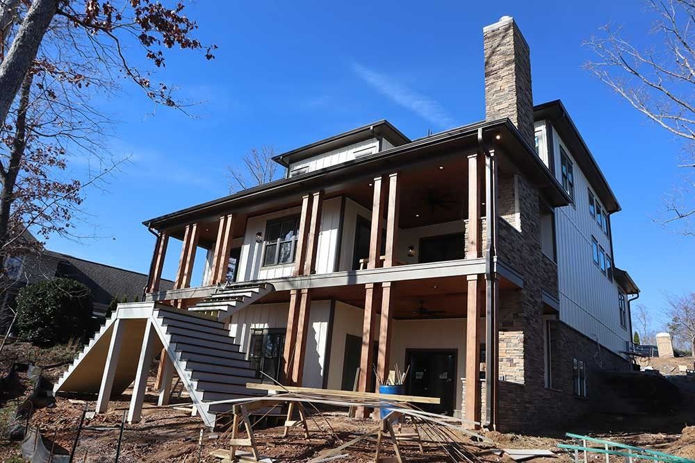 House under construction with porch, exposed framing, and brick chimney on a sunny day
