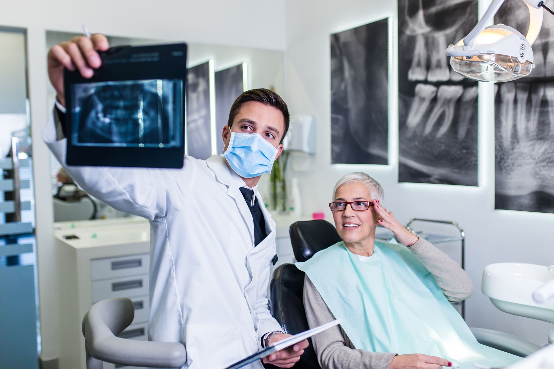 Dentist in mask shows dental x-ray to a patient sitting in a dental chair. 