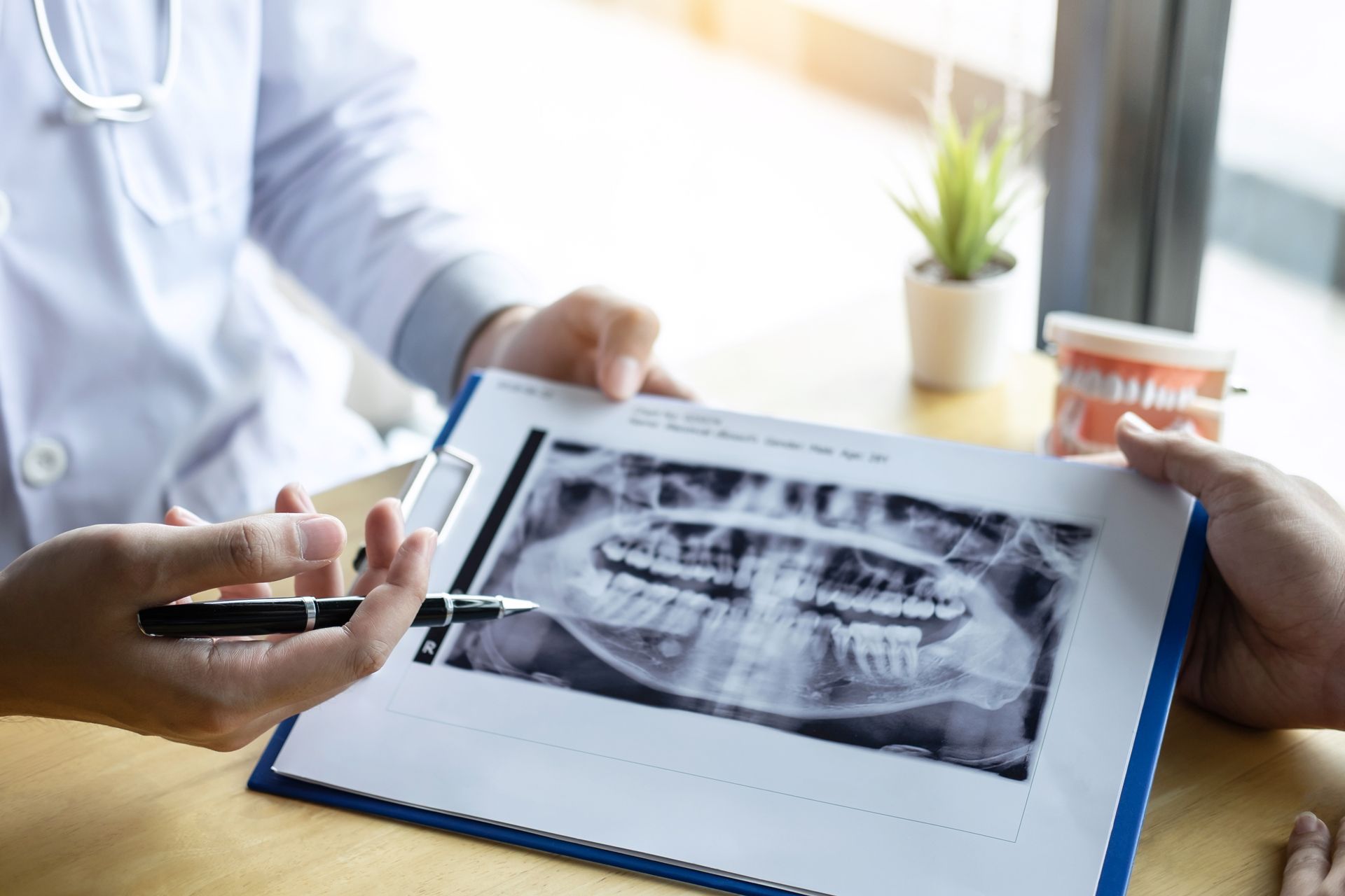 Dentist pointing at patient's panoramic dental X-ray, discussing findings.