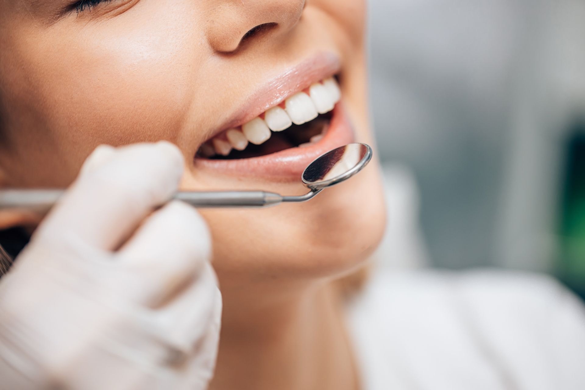 Dentist examining a patient's teeth with a mirror. Patient smiling.