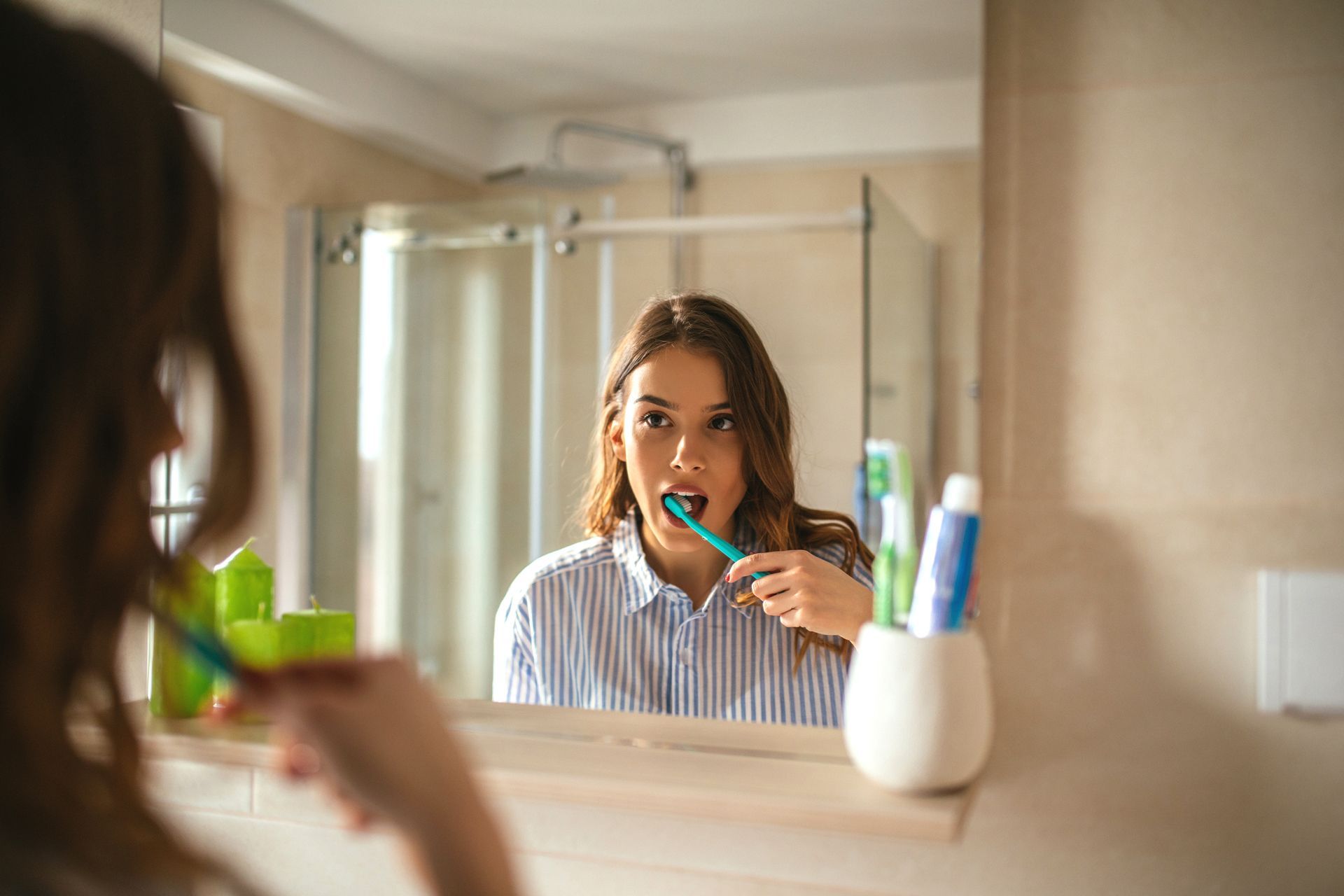 Woman brushing teeth in front of a bathroom mirror, holding a toothbrush.