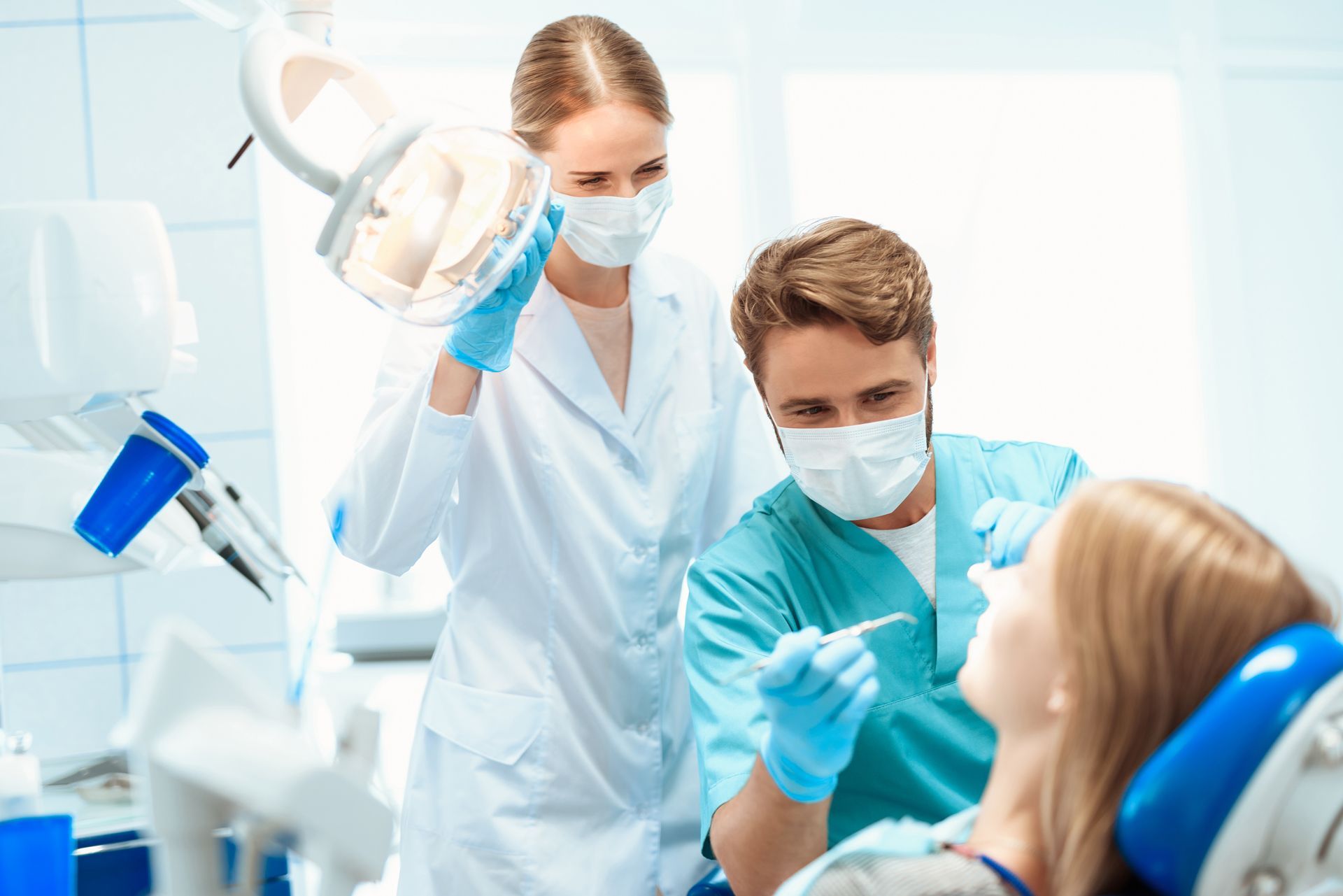 Dentist examining a patient with an assistant in a dental office.