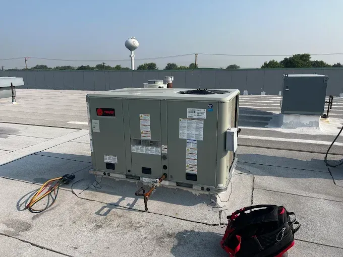 HVAC unit on a flat roof. A toolbox and wires lay nearby. A water tower is in the background.